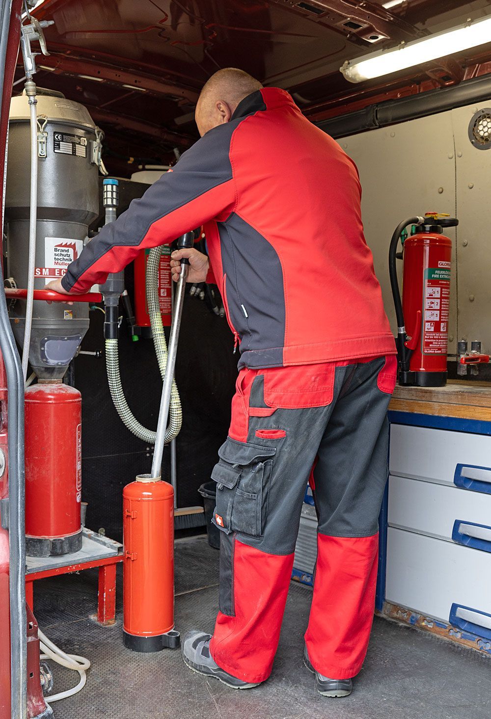 Mann in roter Arbeitskleidung wartet Feuerlöscher in einem Fahrzeug.