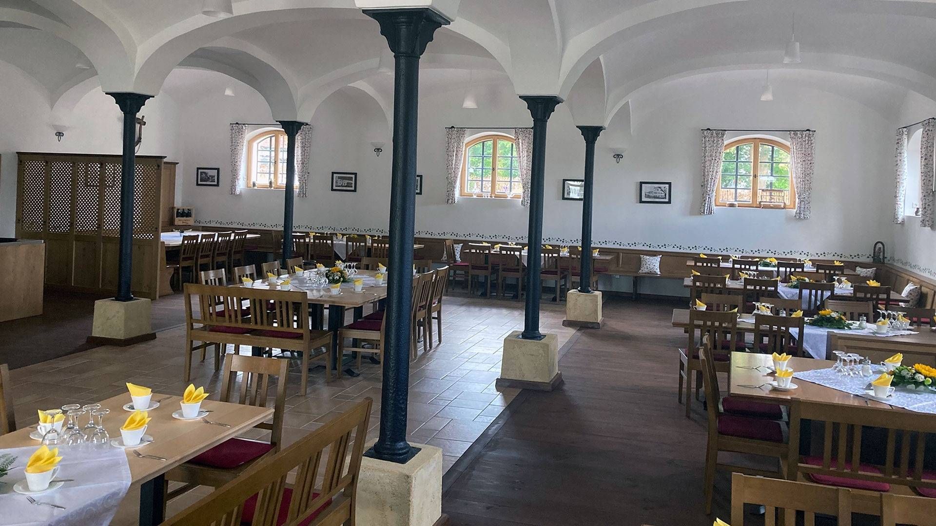 Speisesaal mit gewölbter Decke, Säulen, gedeckten Tischen und Fenstern.