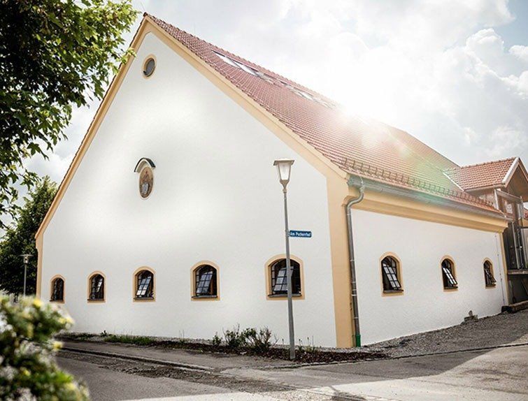 Weißes Gebäude mit rotem Dach, Bogenfenstern und einem Straßenschild an einem sonnigen Tag.