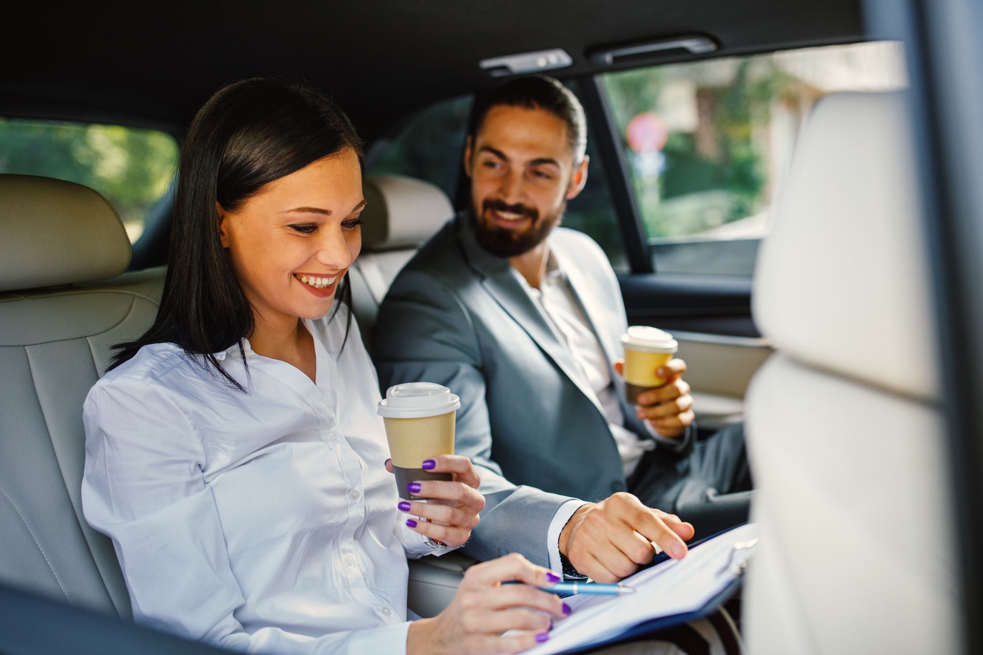 Deux collègues de travail discutent dans un taxi avec un café à la main