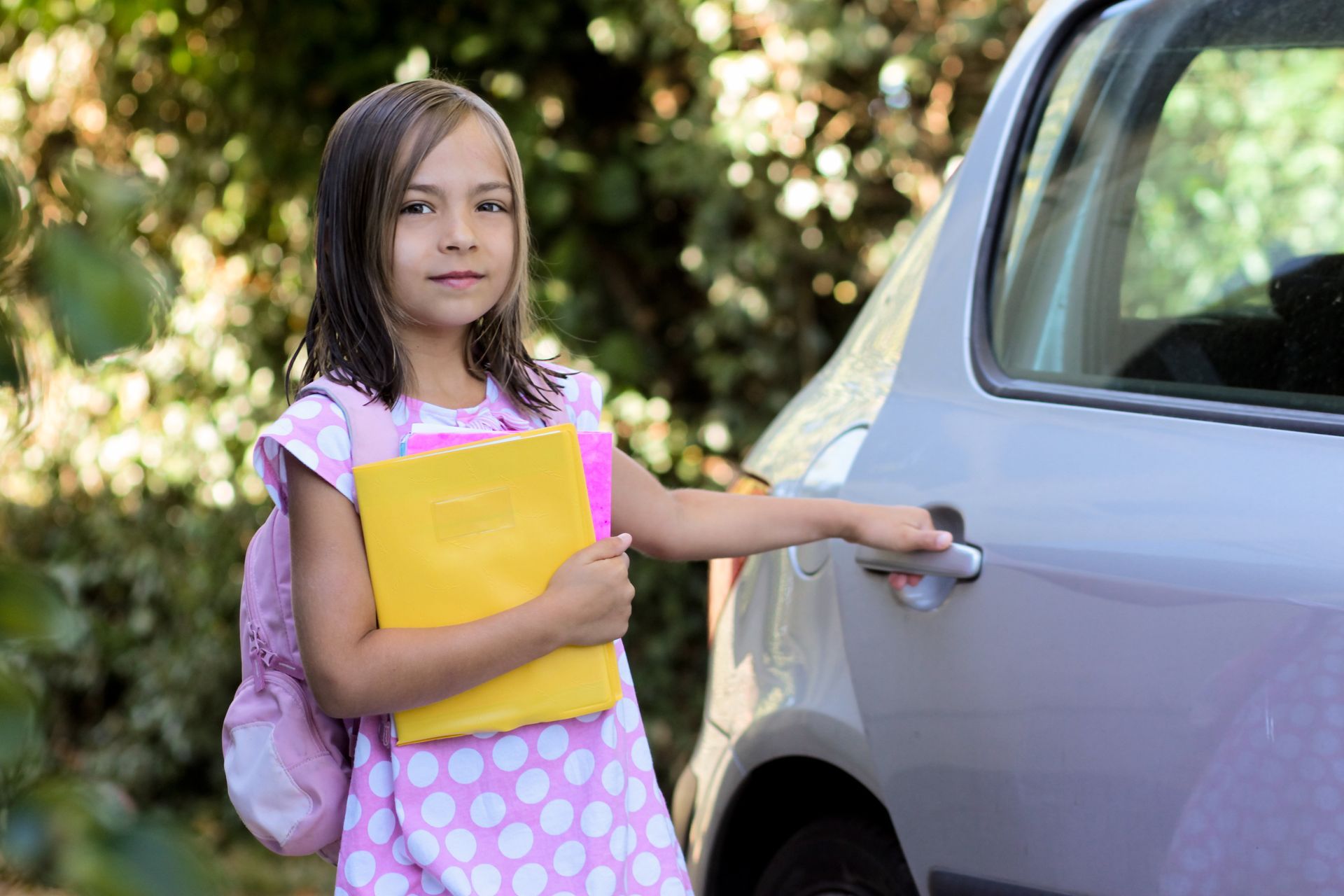 Une petite fille tient des cahiers d’école et ouvre la portière d’une voiture