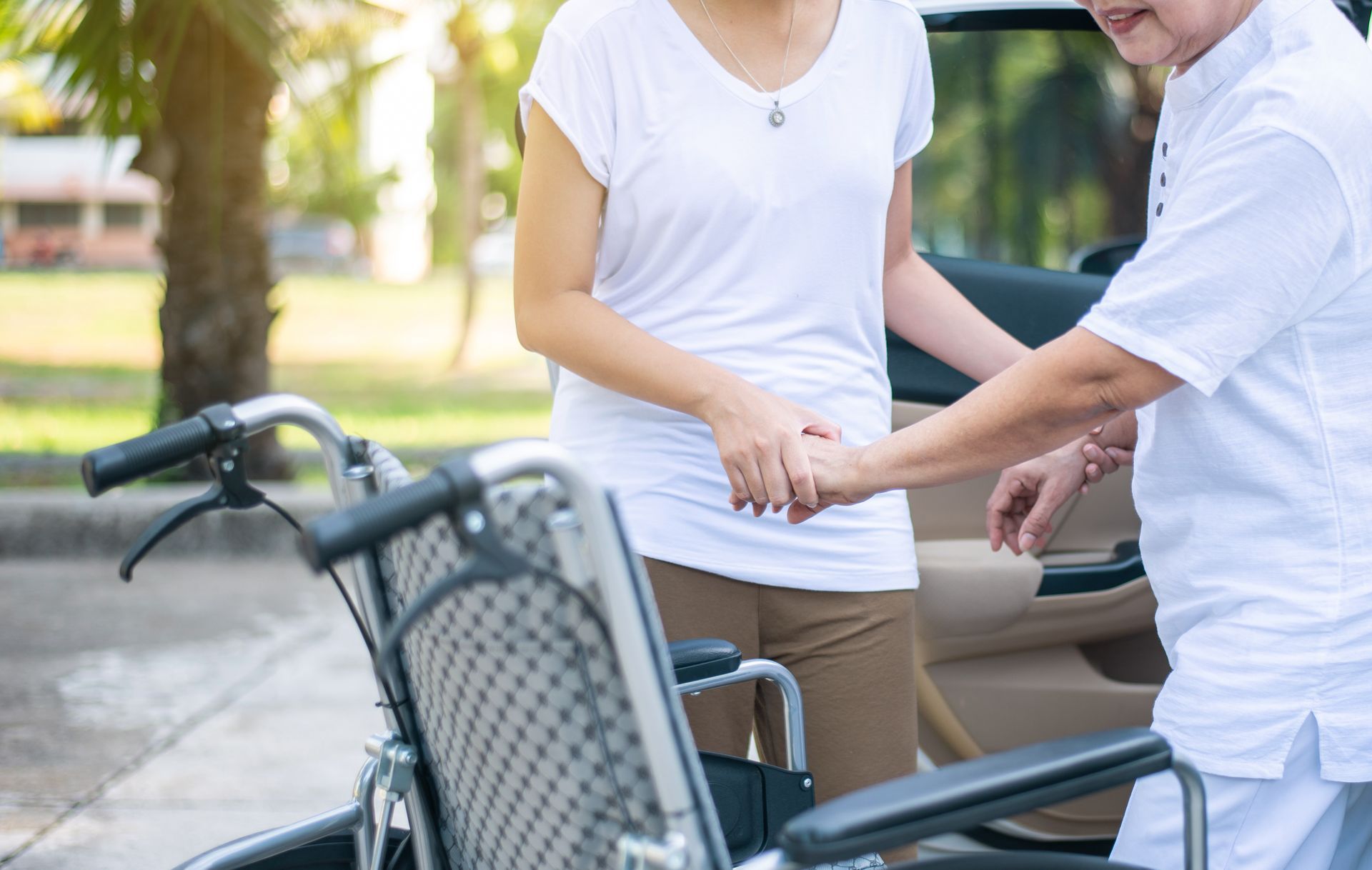 Une femme aide une personne âgée à s’assoir sur un fauteuil roulant à la sortie d’un taxi
