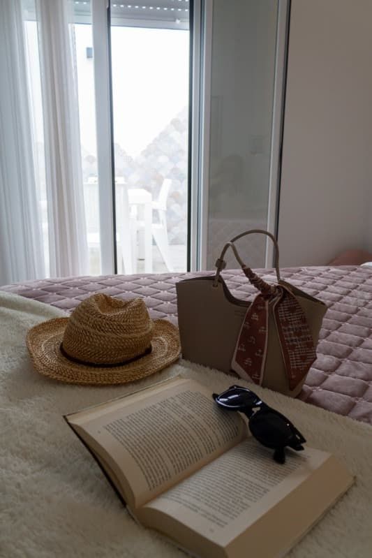 Un sombrero de paja, gafas de sol y un libro están sobre una cama.