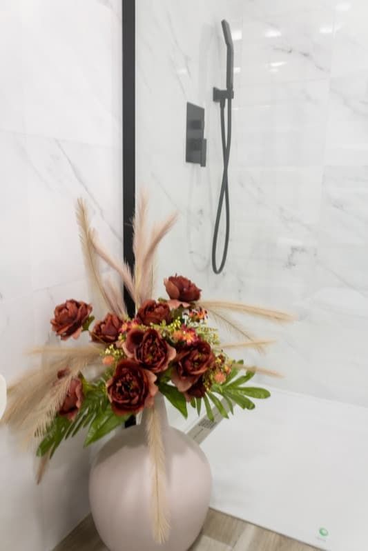 Un jarrón de flores en un baño al lado de una ducha.