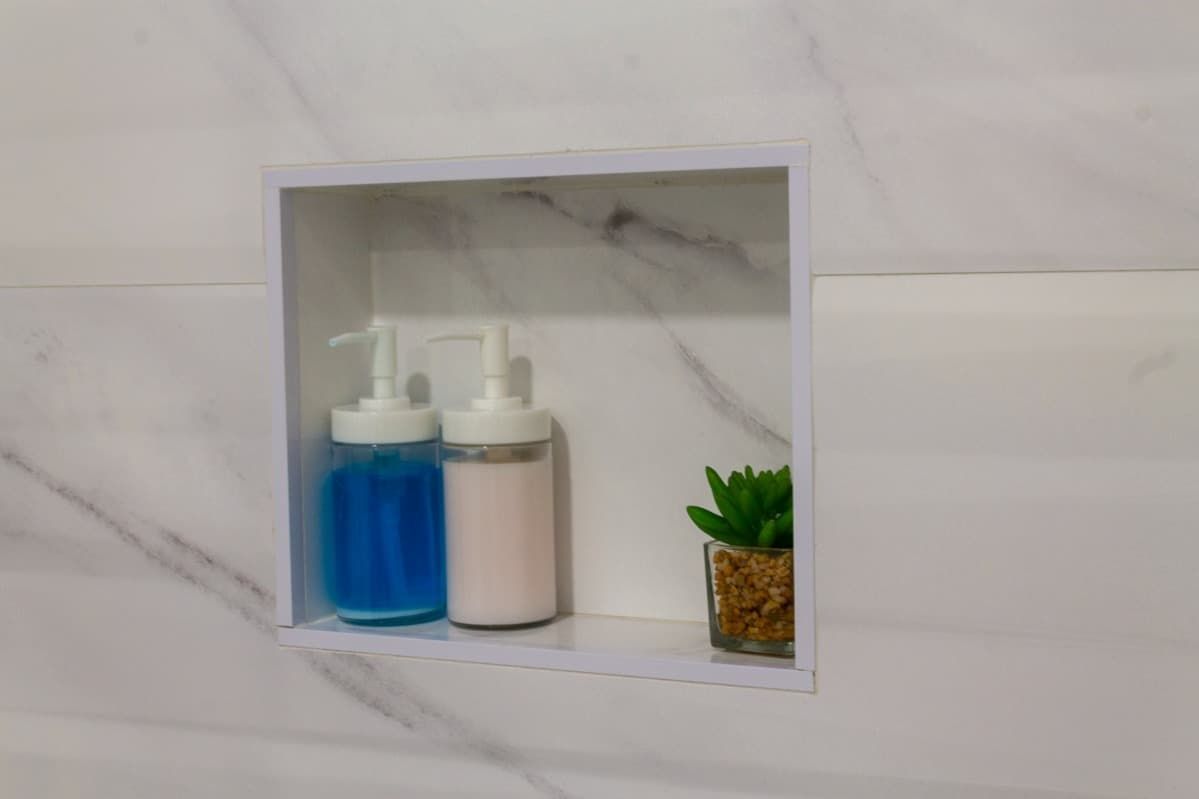 Un estante de baño con dos botellas de jabón y una planta.