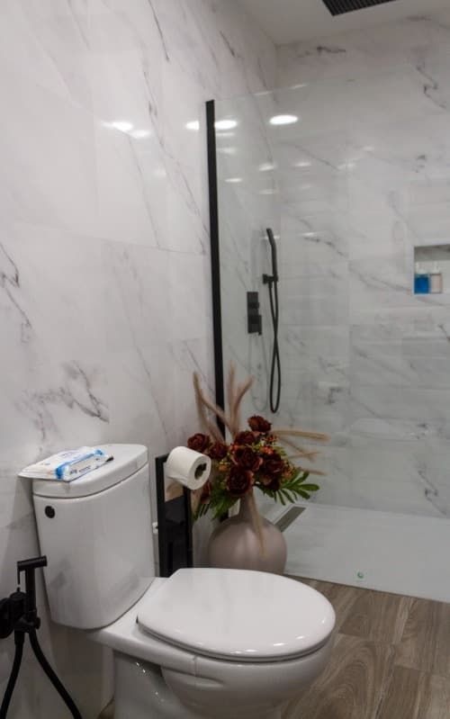 Un baño con inodoro, ducha y jarrón de flores.