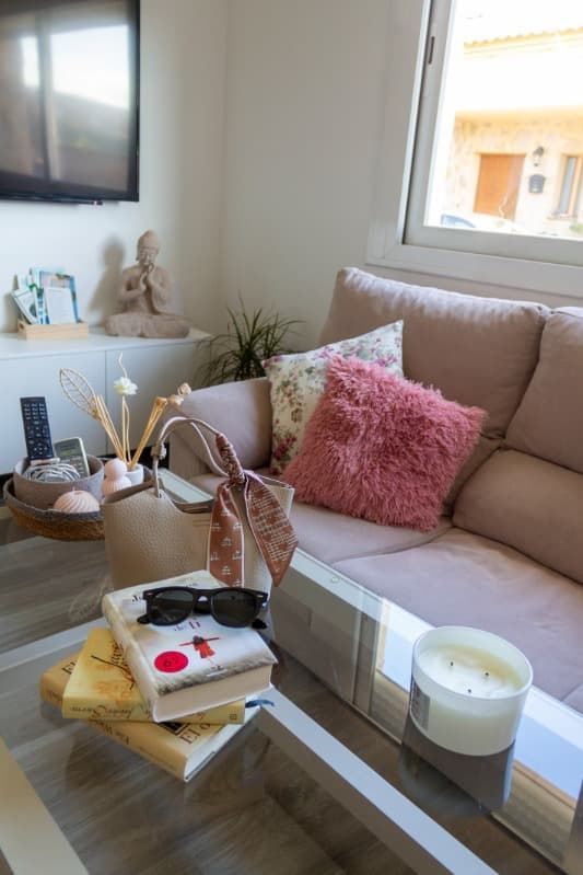Una sala de estar con un sofá, una mesa, libros, gafas de sol y una vela.