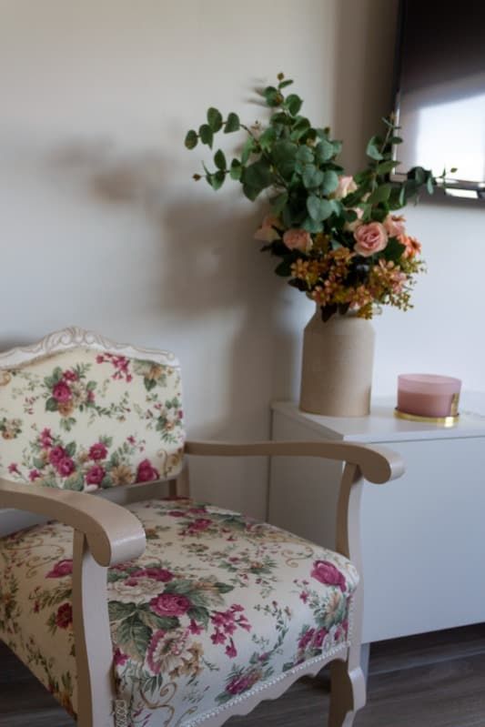 Una silla con un estampado floral se encuentra junto a un jarrón de flores.