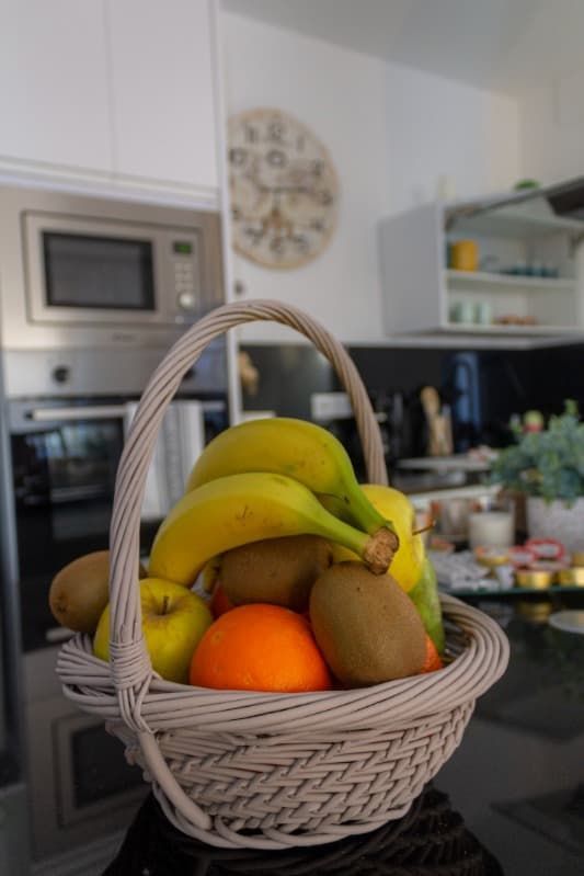 Una cesta llena de fruta está sobre una mesa en una cocina.