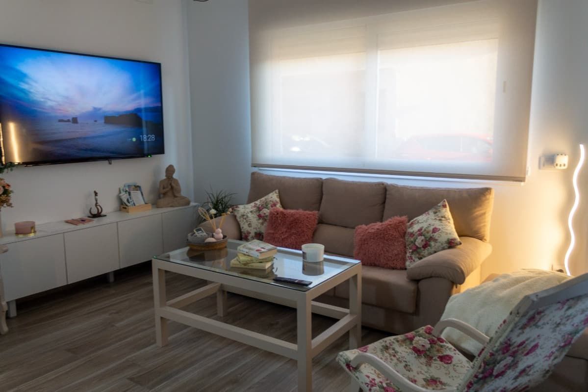 Una sala de estar con sofá, silla, mesa de café y televisión.