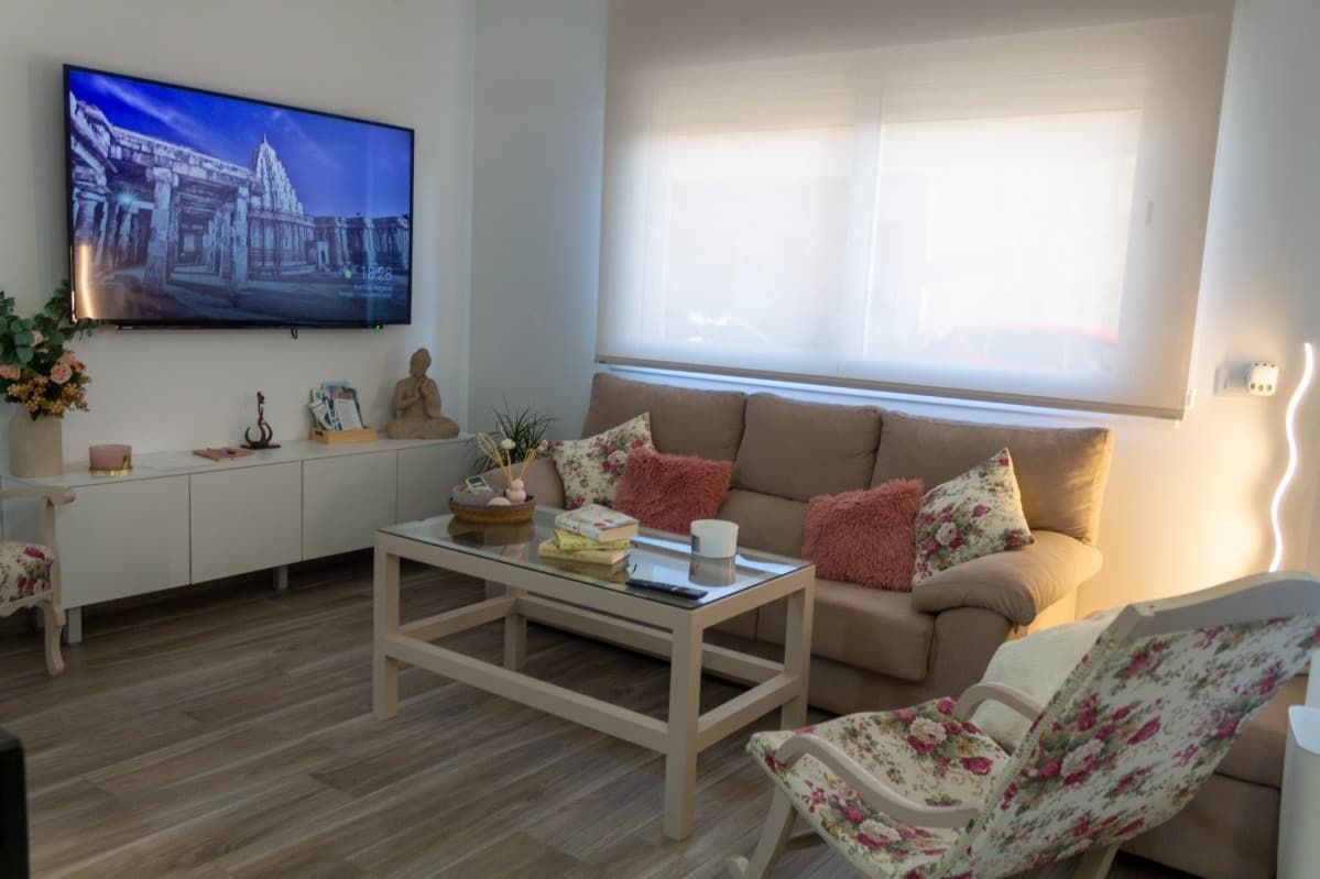 Una sala de estar con sofá, silla, mesa de café y televisión.