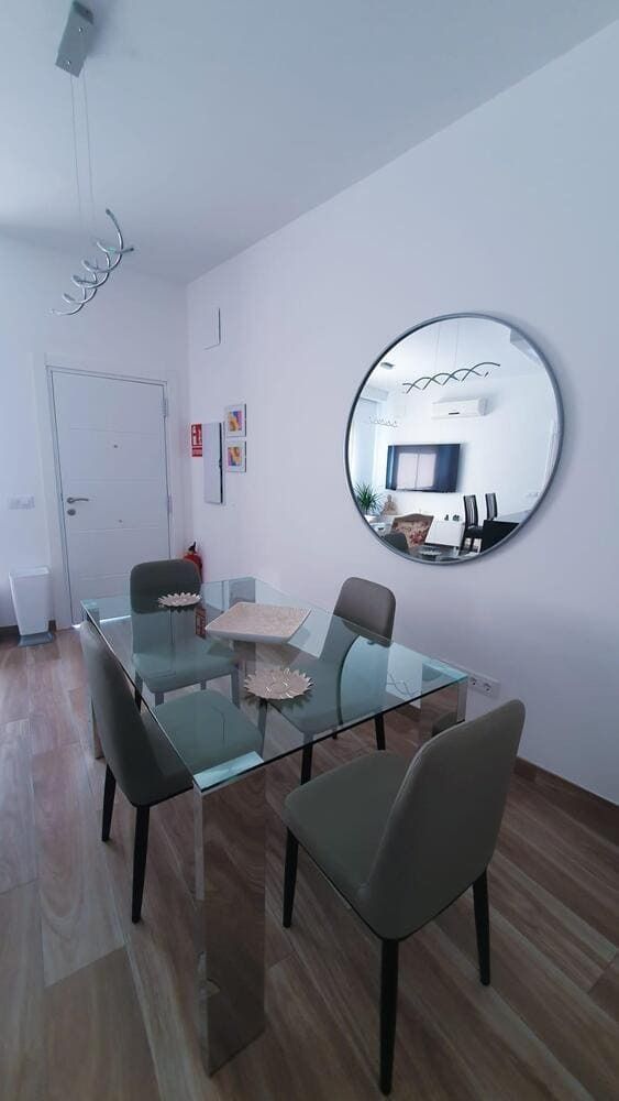 Un comedor con una mesa y sillas de cristal y un espejo redondo en la pared.