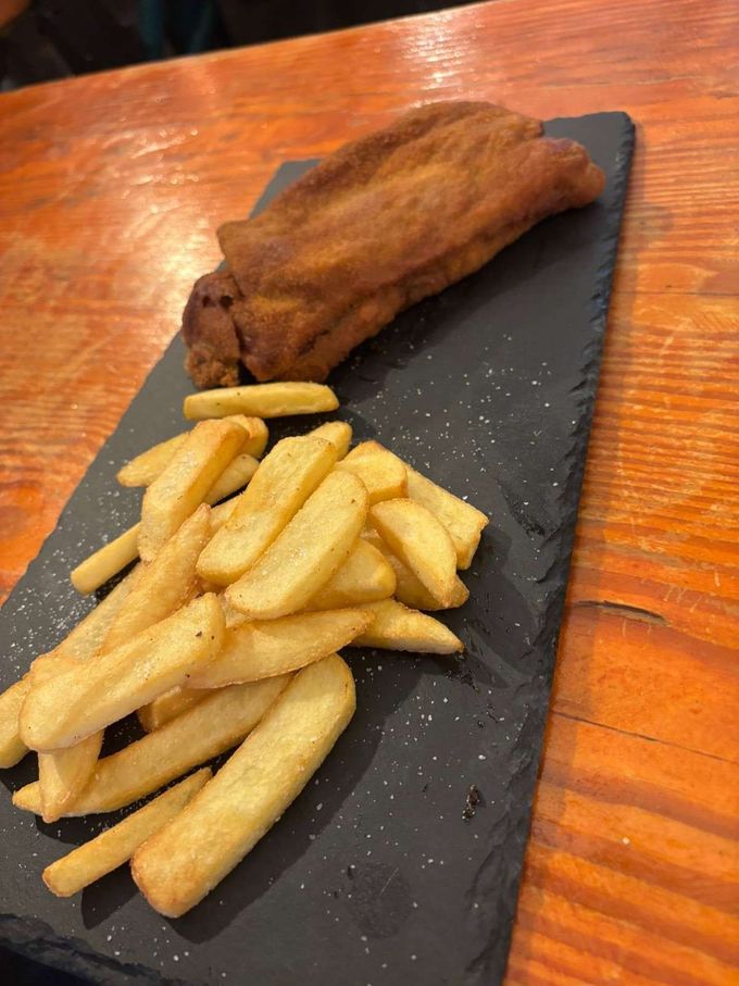 Plato blanco con croquetas empanizadas dispuestas alrededor de pimientos verdes sobre una mesa de madera.