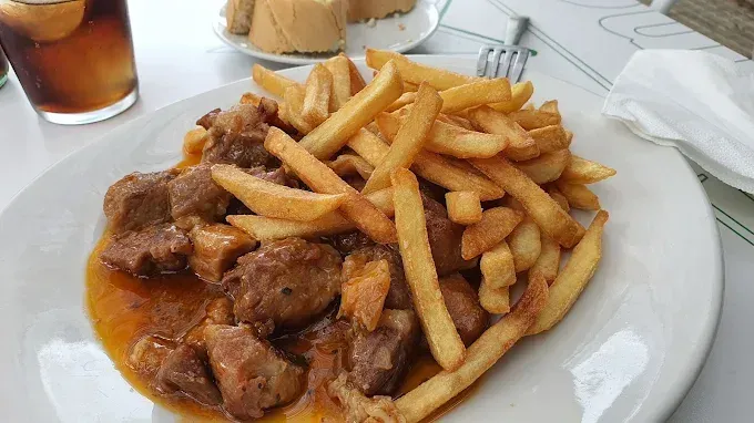 Plato de estofado de ternera con patatas fritas en un plato blanco en la mesa de un restaurante.