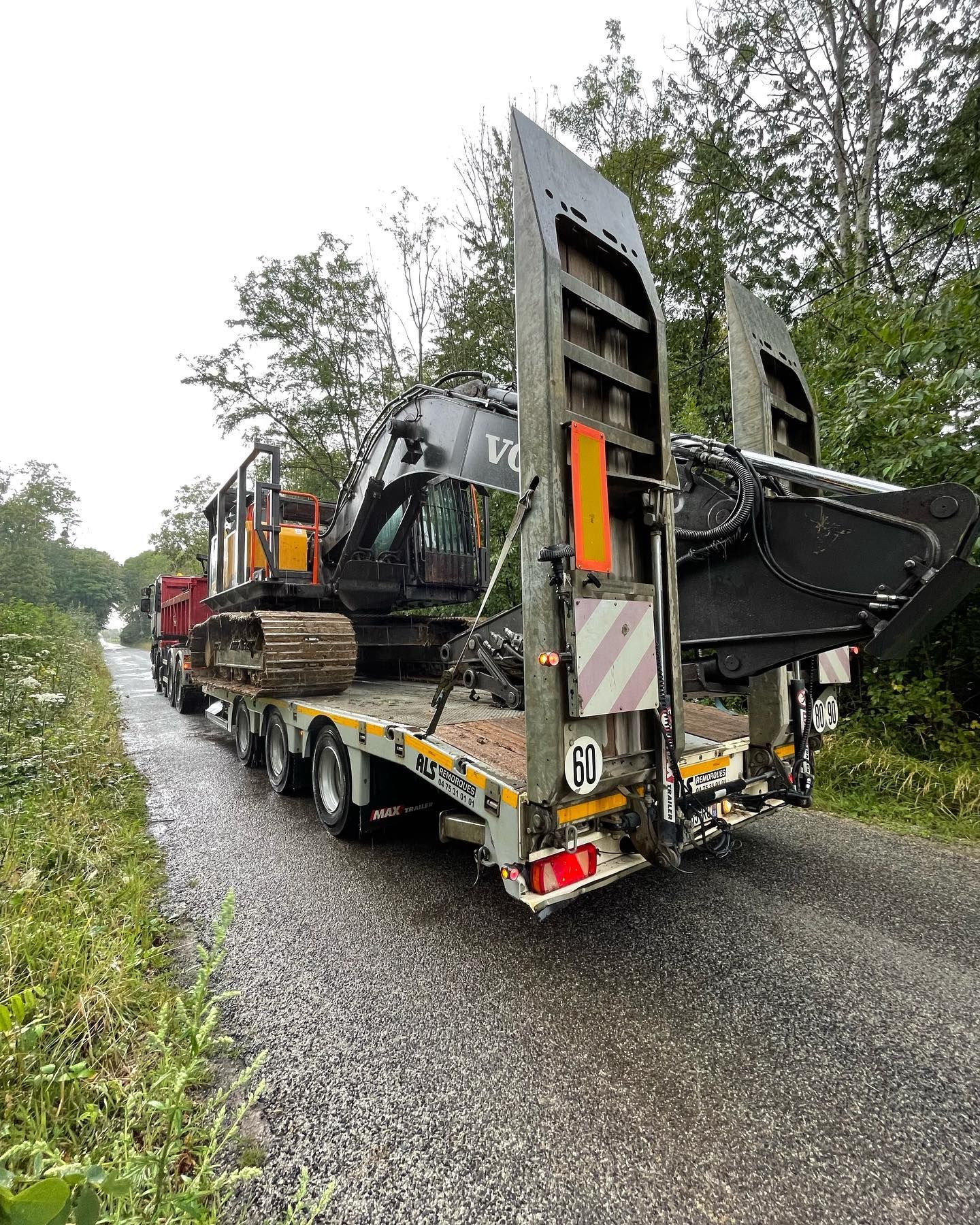 Une excavatrice sur un camion plateau stationnée sur une route de gravier mouillée.