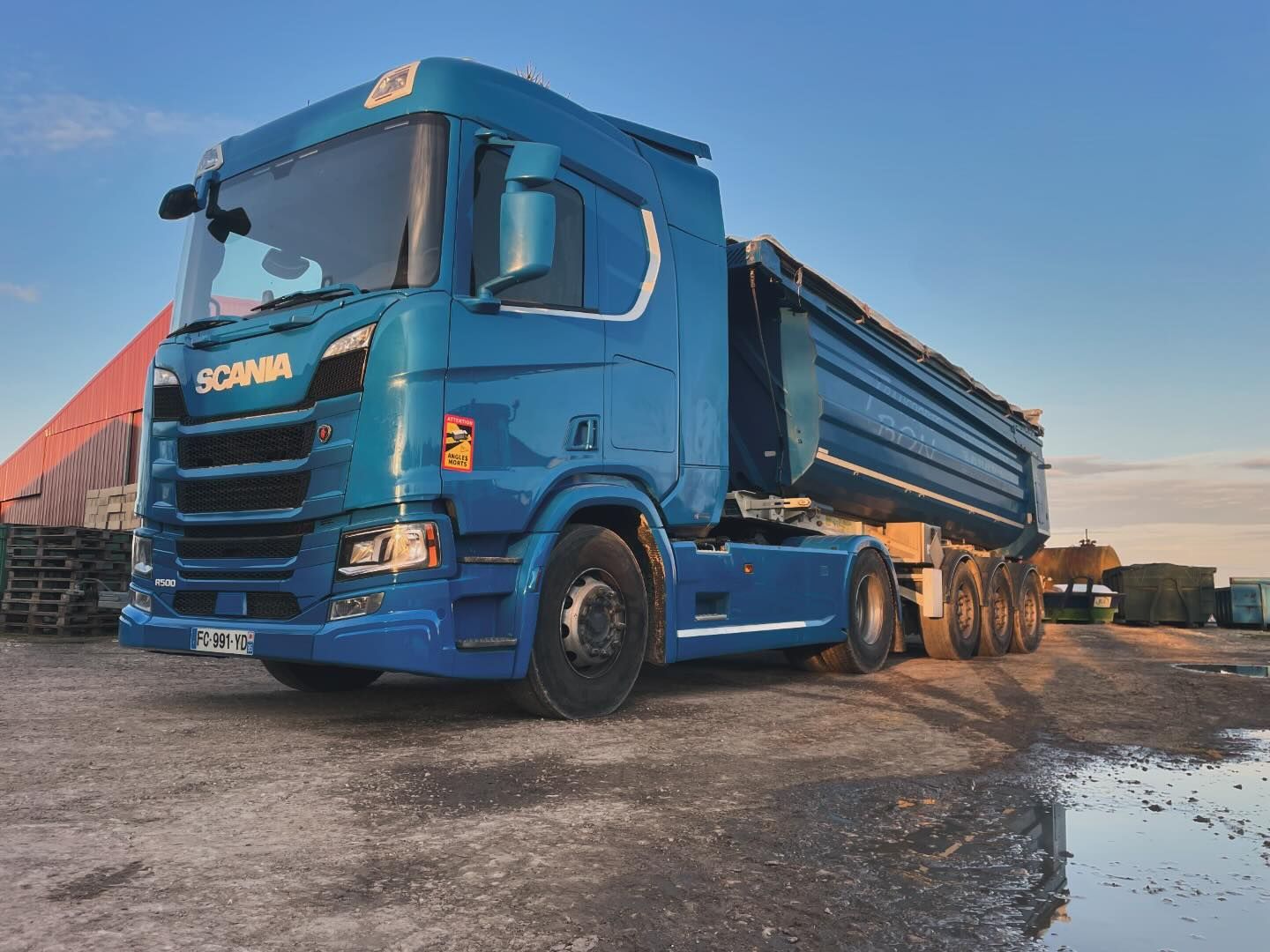 Un camion-benne Scania bleu est stationné sur une surface de gravier.