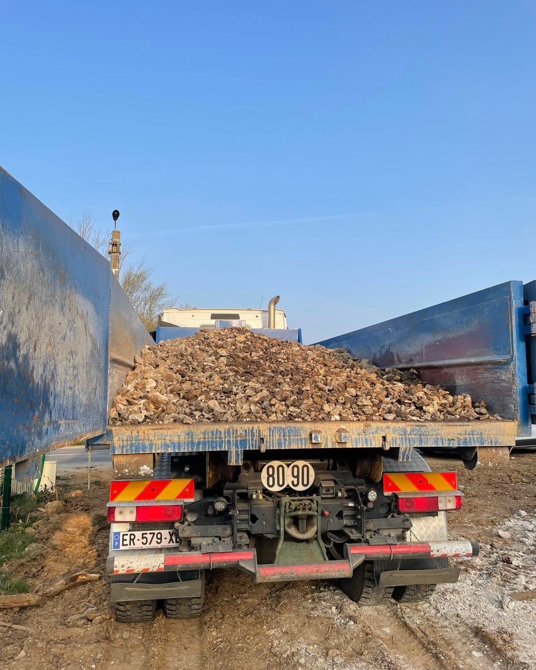Camion-benne chargé de matériaux bruns, stationné sous un ciel bleu.