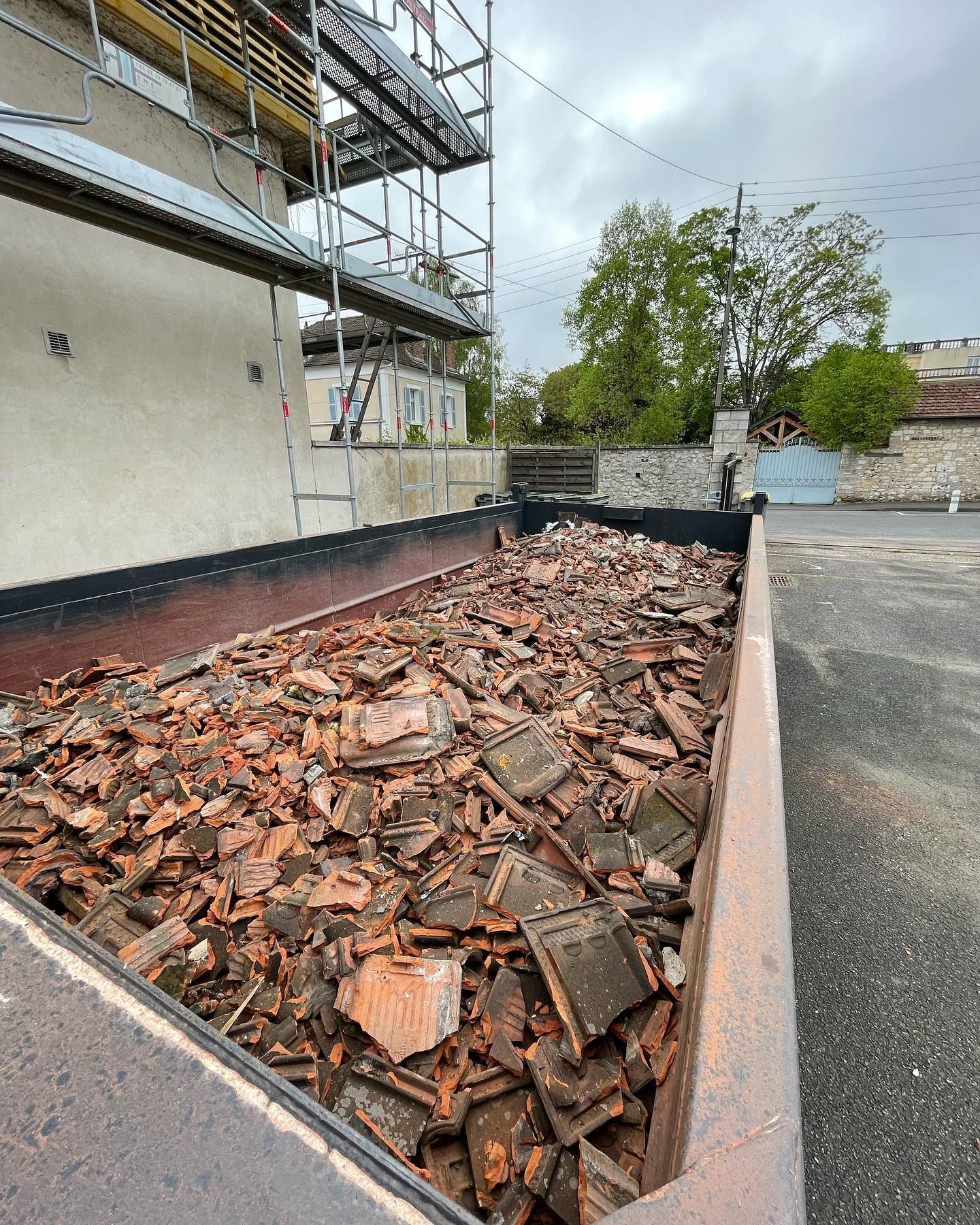 Une benne à ordures débordant de tuiles de toit en terre cuite cassées.