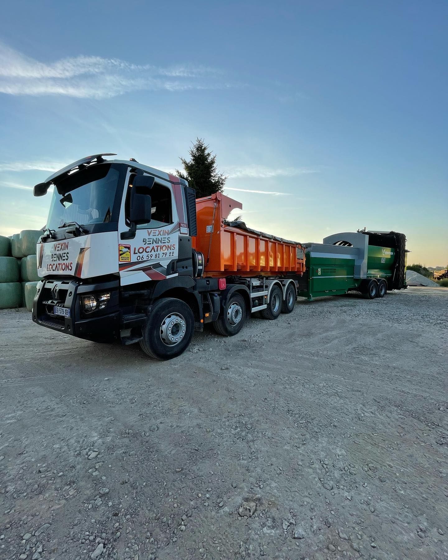 Camion à benne basculante orange et remorque verte sur du gravier, sur fond de ciel bleu.