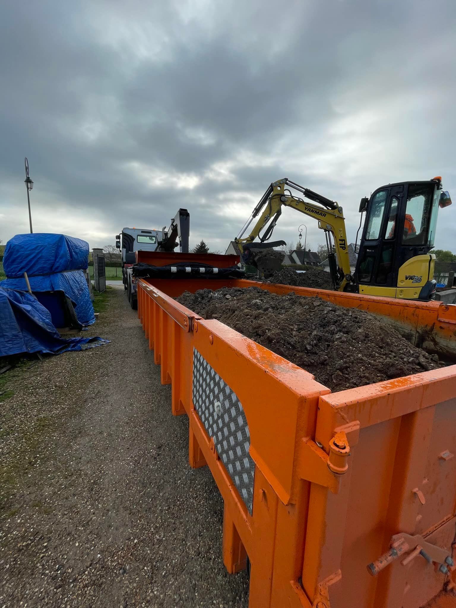 Un camion-benne orange est rempli de terre par une excavatrice.