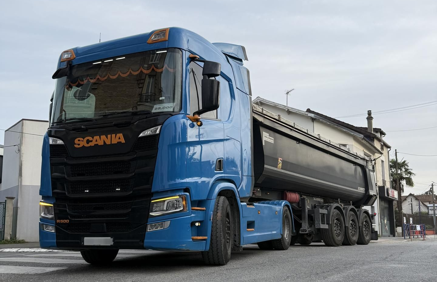 Camion Scania bleu et noir avec une benne à marchandises dans une rue.