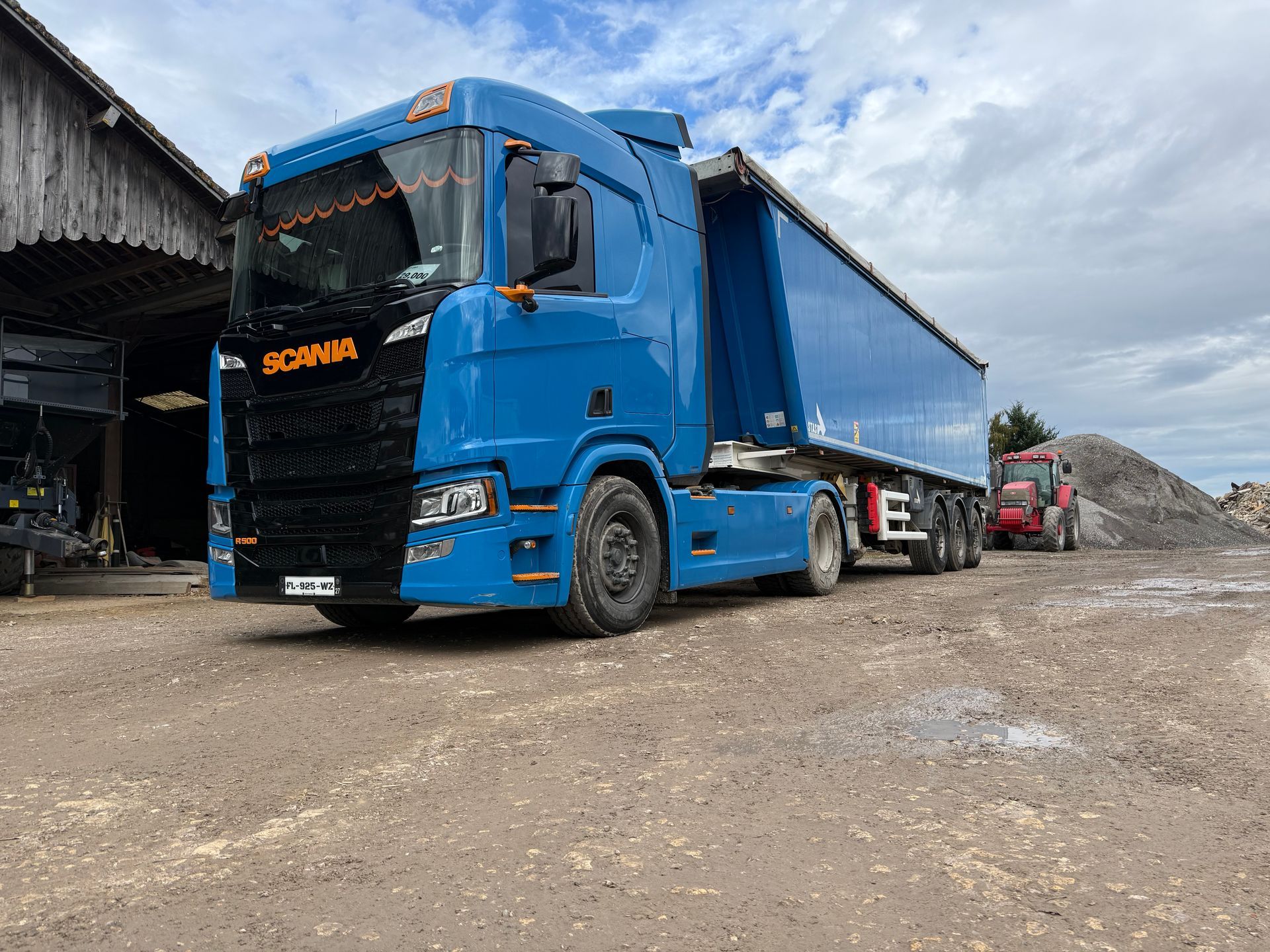 Un tracteur noir tirant une remorque rouge dans un champ de récoltes.