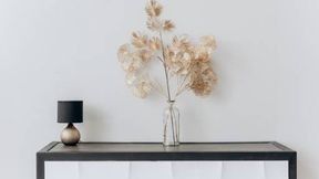 Un jarrón de flores secas está sobre una mesa al lado de una lámpara.
