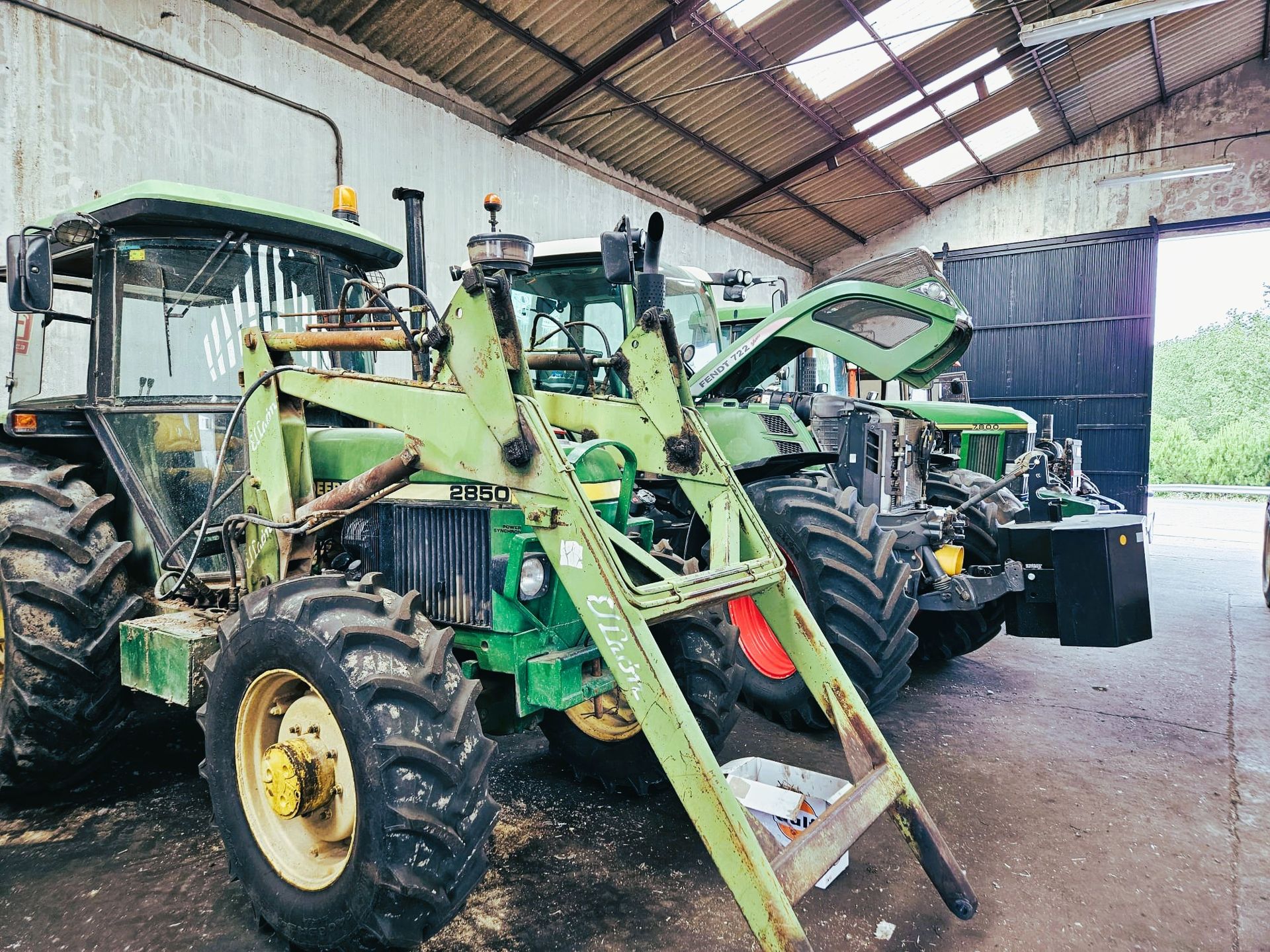 Una fila de tractores verdes están estacionados en un granero.