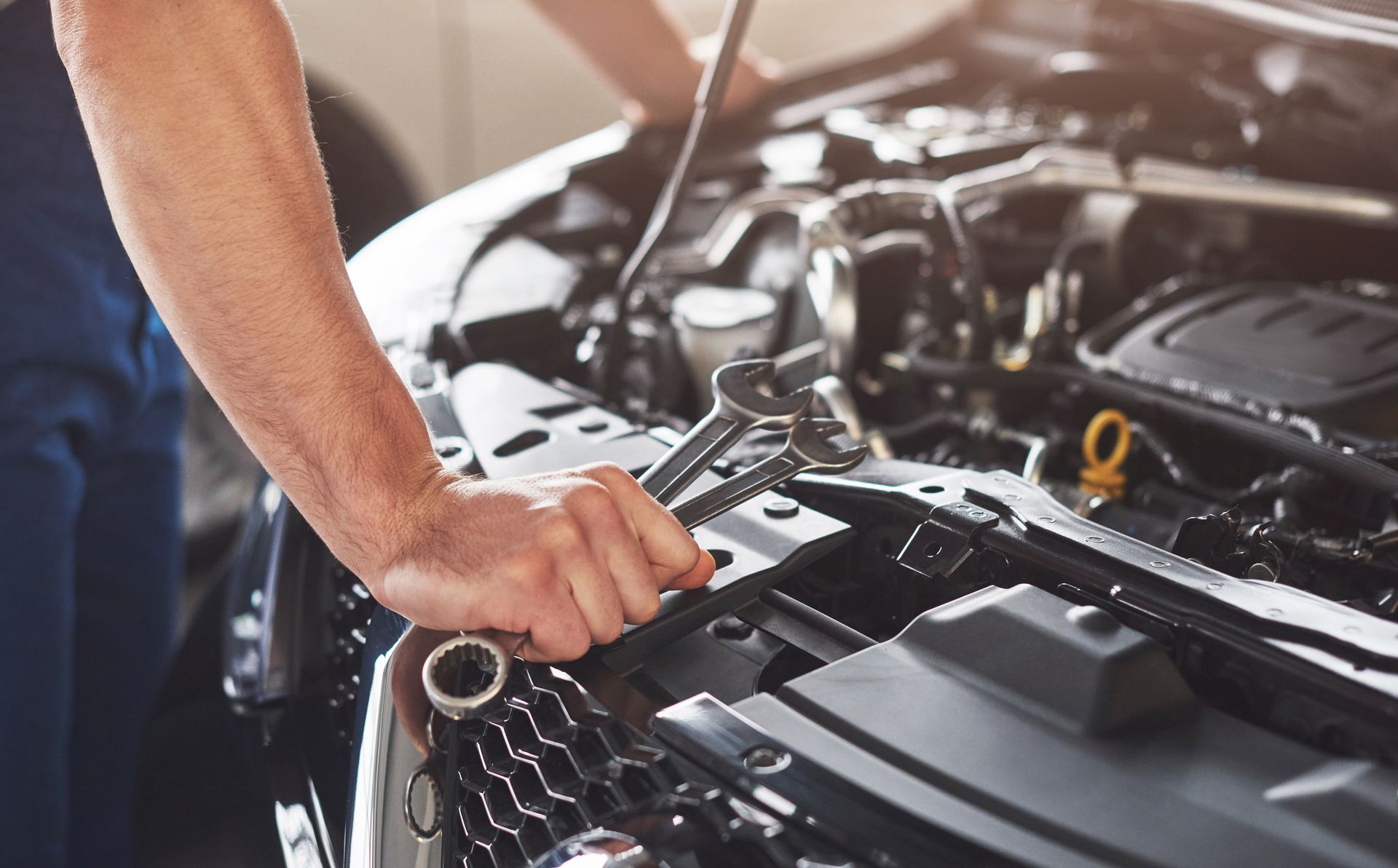 Un hombre está trabajando en el motor de un automóvil con una llave inglesa.