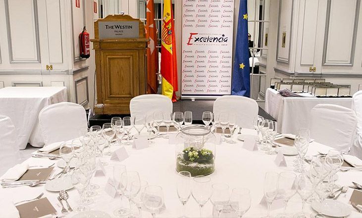 Elegante mesa de banquete con sillas blancas, cristalería y centros de mesa florales en un comedor formal.