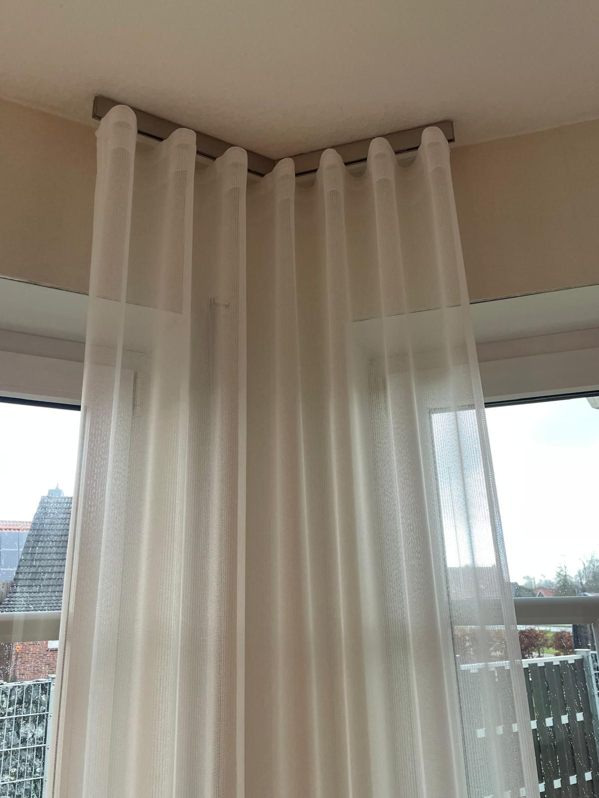 Ein Paar weiße Vorhänge, die neben einem Fenster von der Decke hängen.