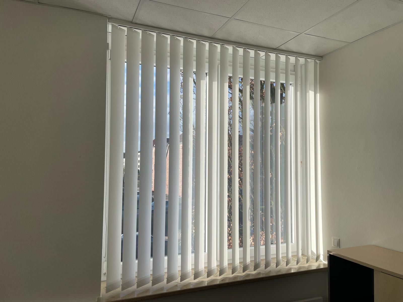 Ein Raum mit weißen Vertikaljalousien an einem Fenster.