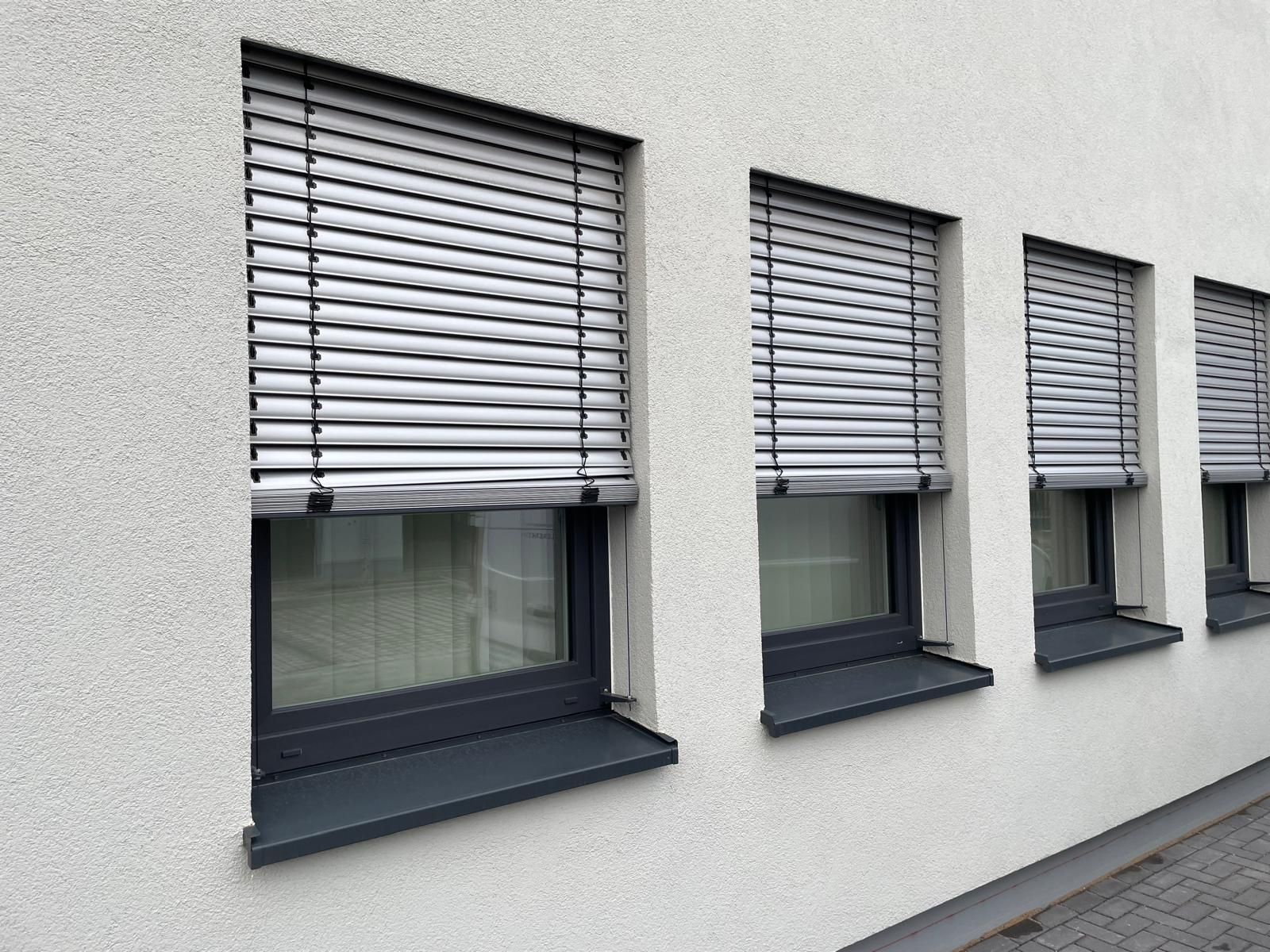 Eine Reihe von Fenstern mit Jalousien an der Seite eines Gebäudes.