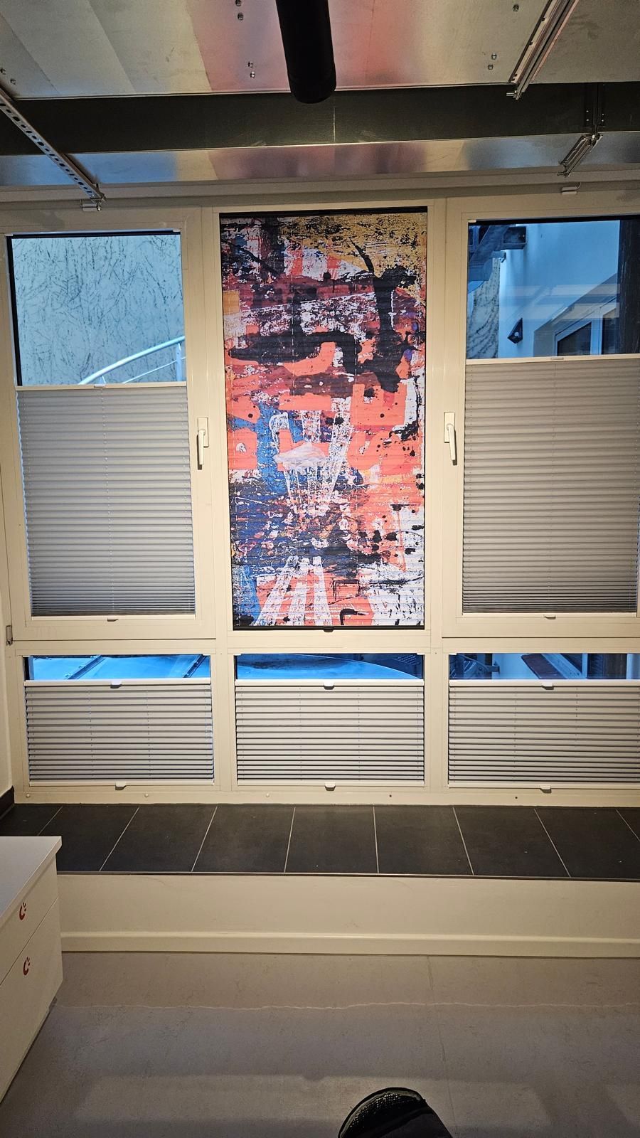 Ein Fenster mit Jalousien und einem Gemälde darauf in einem Zimmer.