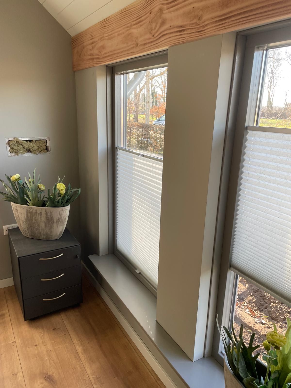 Ein Zimmer mit einem Fenster und einer Vase mit Blumen auf einem Nachttisch.