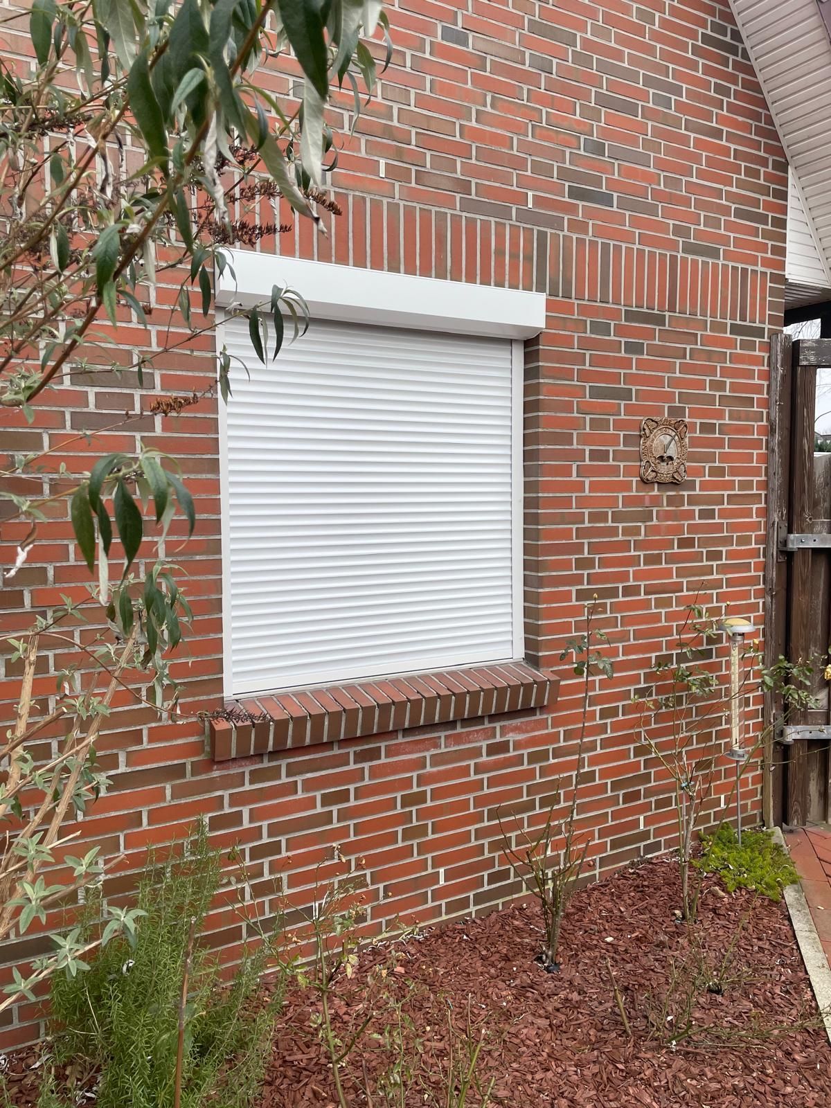 Ein Backsteingebäude mit einem weißen Rollladen am Fenster.