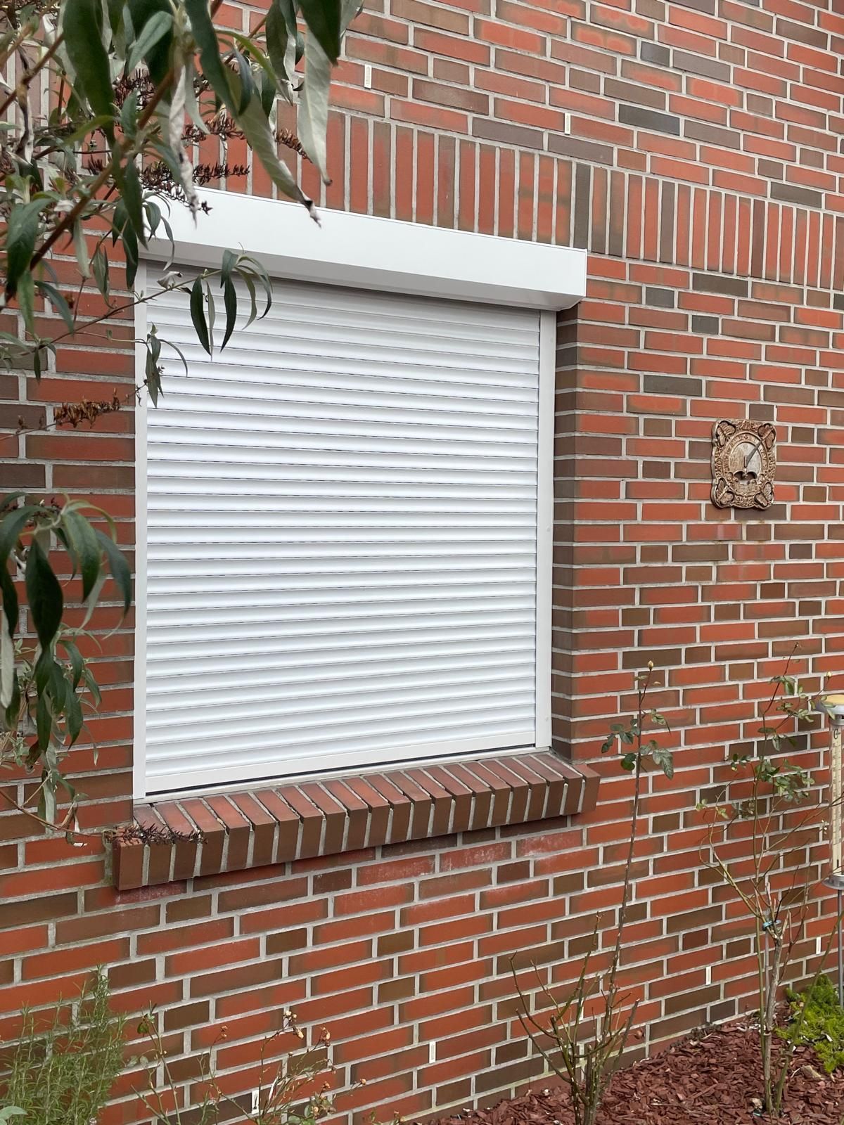 Eine Backsteinmauer mit einem Fenster mit einem weißen Rollladen daran.