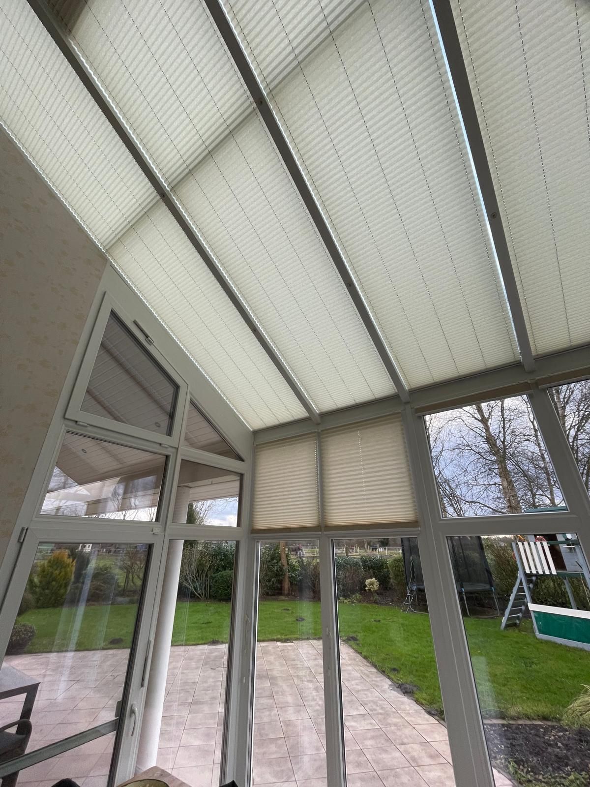 Ein Wintergarten mit Jalousien an der Decke und einer Terrasse im Hintergrund.