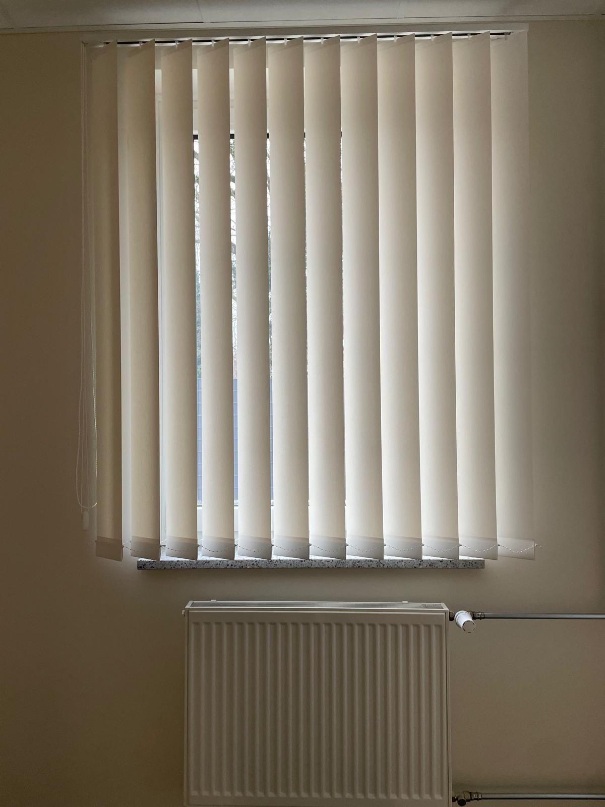 Ein Fenster mit Vertikaljalousien und einem Heizkörper in einem Zimmer.