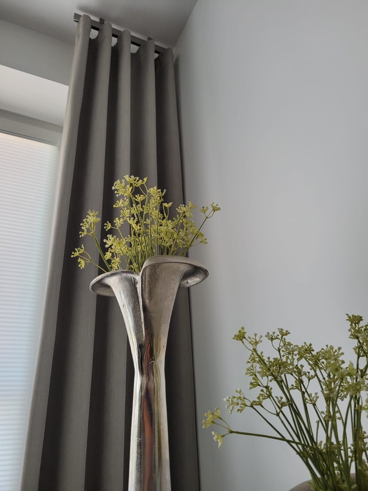 Eine silberne Vase mit Blumen steht vor einem Fenster.