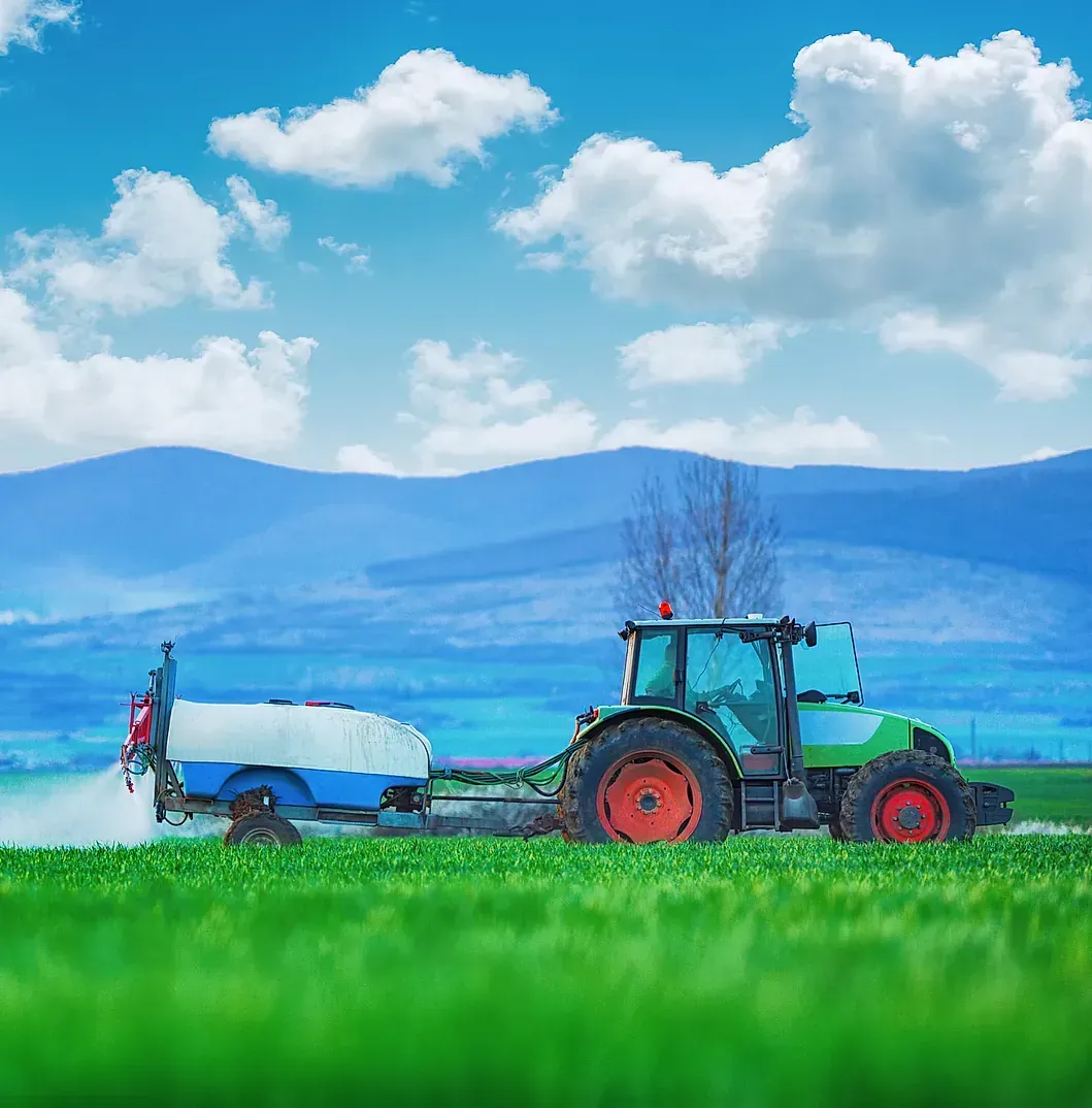 Un tractor está rociando fertilizante en un exuberante campo verde.