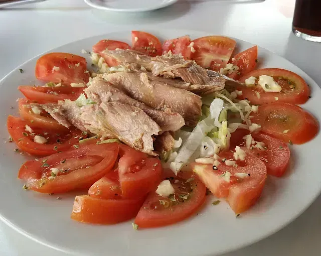 Un plato blanco cubierto con tomates y carne sobre una mesa.