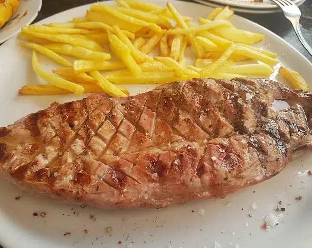 Un plato blanco cubierto con un filete y papas fritas.