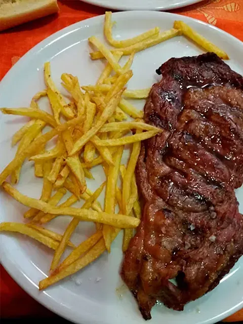 Un plato blanco cubierto con un bistec y papas fritas