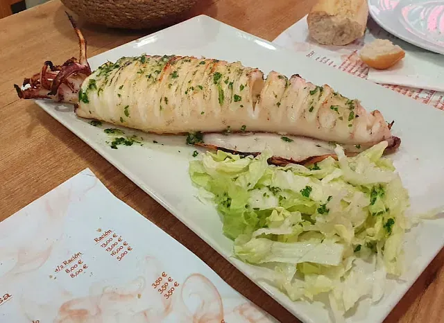 Un plato blanco con un calamar y lechuga encima.