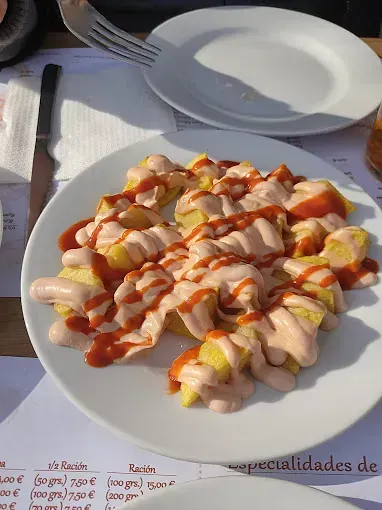 Un plato blanco cubierto con papas fritas y salsa sobre una mesa.