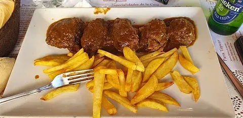 Un plato blanco cubierto con albóndigas y papas fritas con un tenedor.