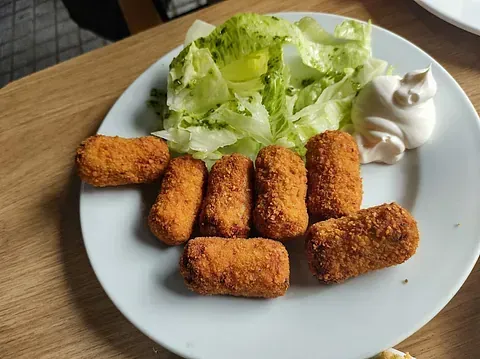 Un plato blanco cubierto con comida frita y una ensalada sobre una mesa.