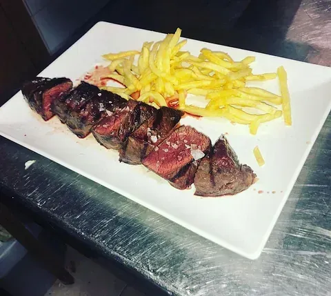 Un plato blanco cubierto con bistec y papas fritas
