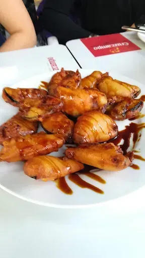 Un plato blanco cubierto con alitas de pollo y salsa sobre una mesa.